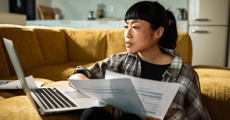 Woman sitting by the couch with a laptop and papers in her hand