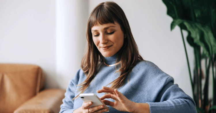 Seated woman smiling down at her smartphone.