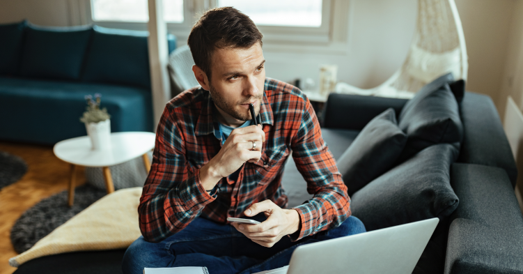 Man sitting at laptop with a pen and his phone thinking about finances