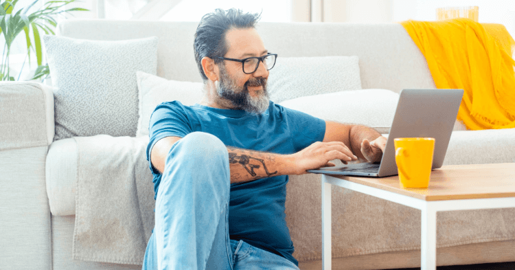 Man sitting in front of couch looking at online banking on his laptop