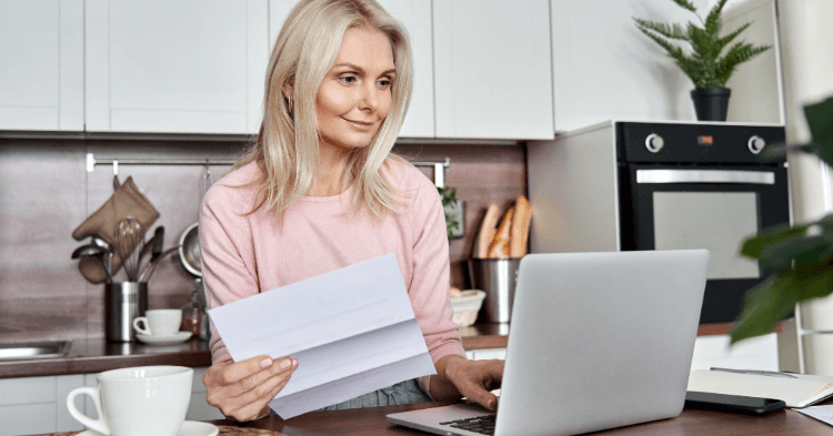 Woman at a laptop holding a paper and making a budget