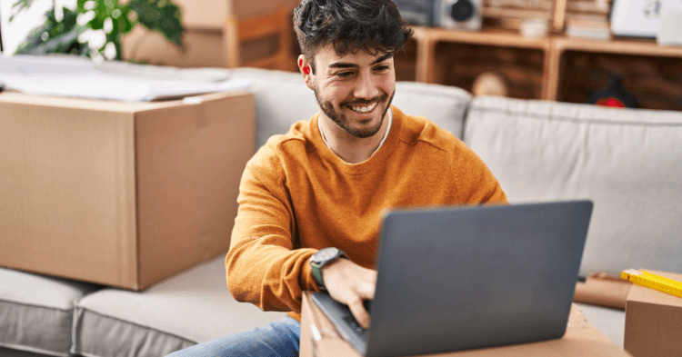 Young man looking at his laptop while sitting on the couch with moving boxes