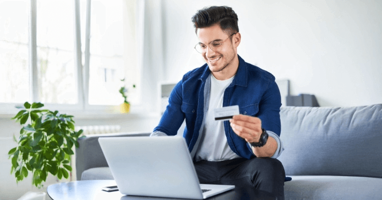 Man sitting on his couch at a coffee table with a laptop holding a credit card
